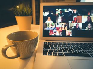 Laptop mit Online-Meeting, daneben steht eine Tasse
